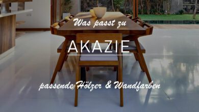 Zu sehen ist ein Ausschnitt aus einer Küche und einem Esszimmer. Ein langgezogener Tisch wird von insgesamt 8 Stühl umsäumt - alle aus Akazienholz gefertigt. Das Esszimmer ist in Weiß gefließt. Dazu erkennt man zwei beige Schalen in der Mitte des Tisches, welche die Farbe der Stoffbezüge der Stühle mit aufgreift. Das Bild ist allgemein abgedunkelt, um den Titel besser zu erkennen: Was passt zu Akazie? Passende Hölzer und Wandfarben.